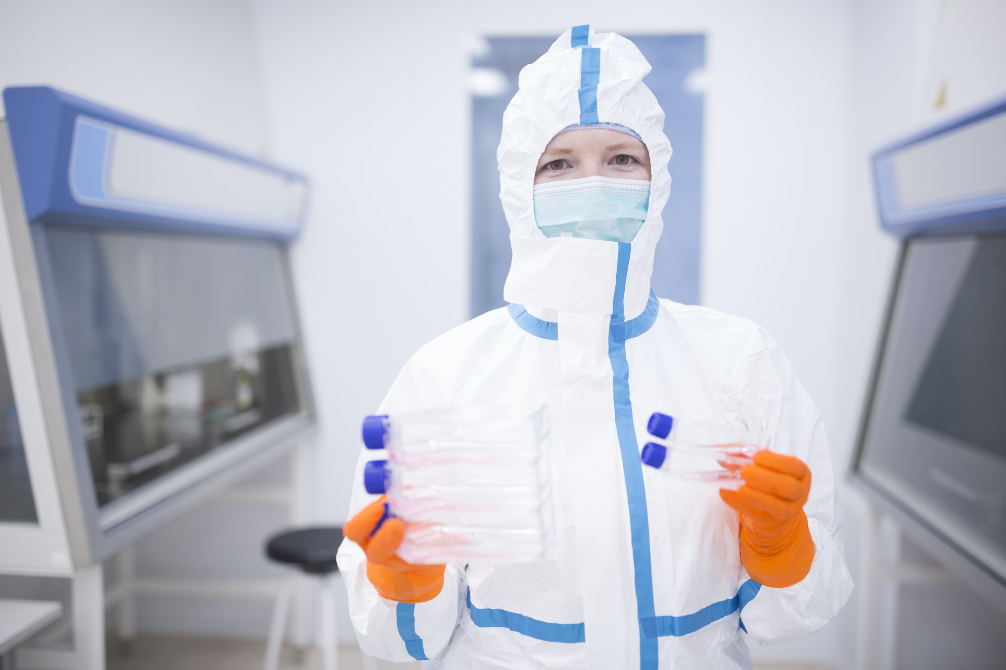 Lab technician wearing cleanroom overall holding cultivation containers
